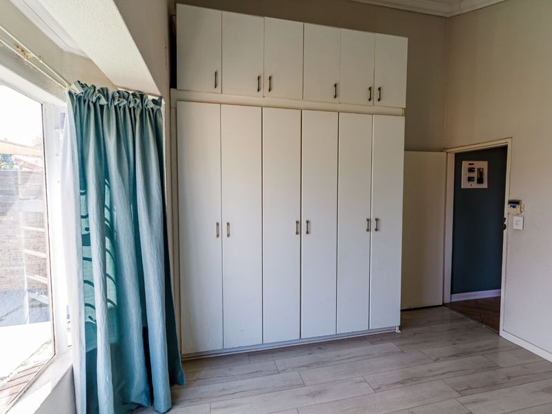 A bright bedroom featuring extensive floor-to-ceiling built-in cupboards, light-toned laminate flooring, and neutral wall finishes, offering a clean and functional space.