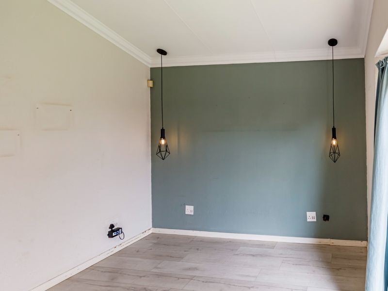 An empty bedroom featuring laminate flooring, a green accent wall, and modern pendant lighting, ready for personalization.
