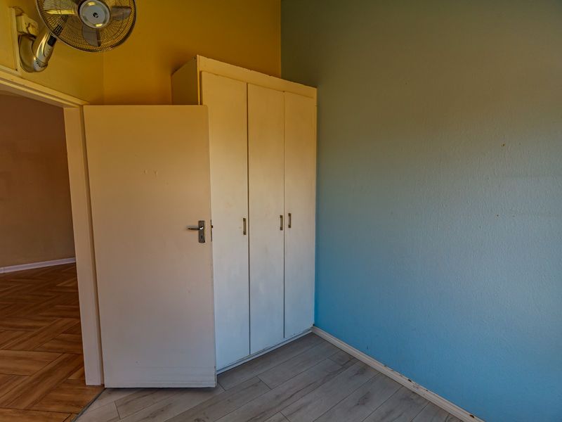 A vacant bedroom featuring built-in wardrobes, laminate flooring, and blue accent wall paint, requiring minor cosmetic updates.
