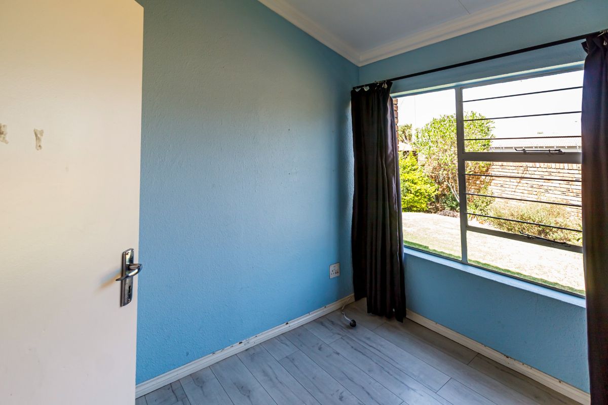 An empty bedroom featuring light-toned laminate flooring, blue painted walls, and a window fitted with security bars.