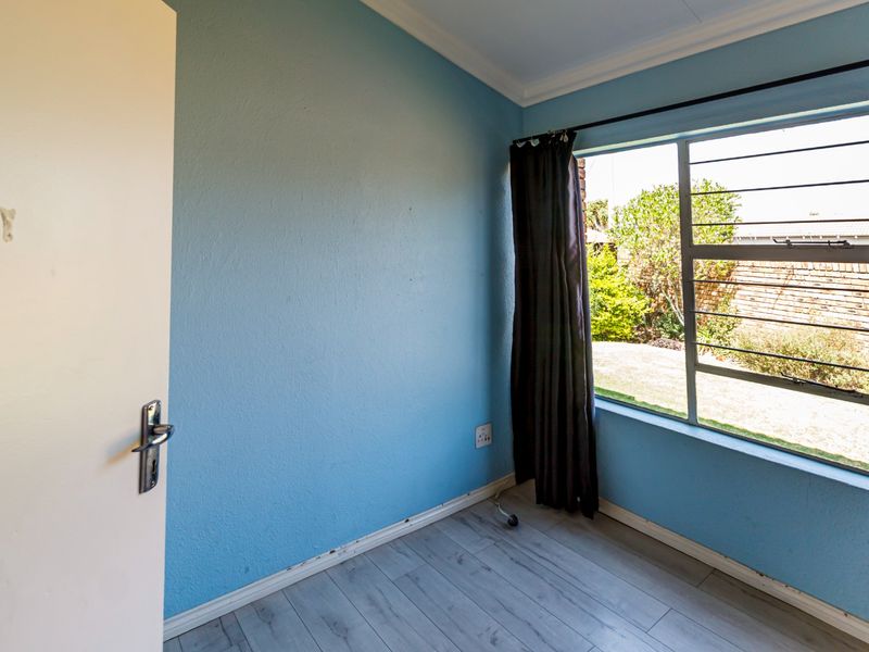 An empty bedroom featuring light-toned laminate flooring, blue painted walls, and a window fitted with security bars.