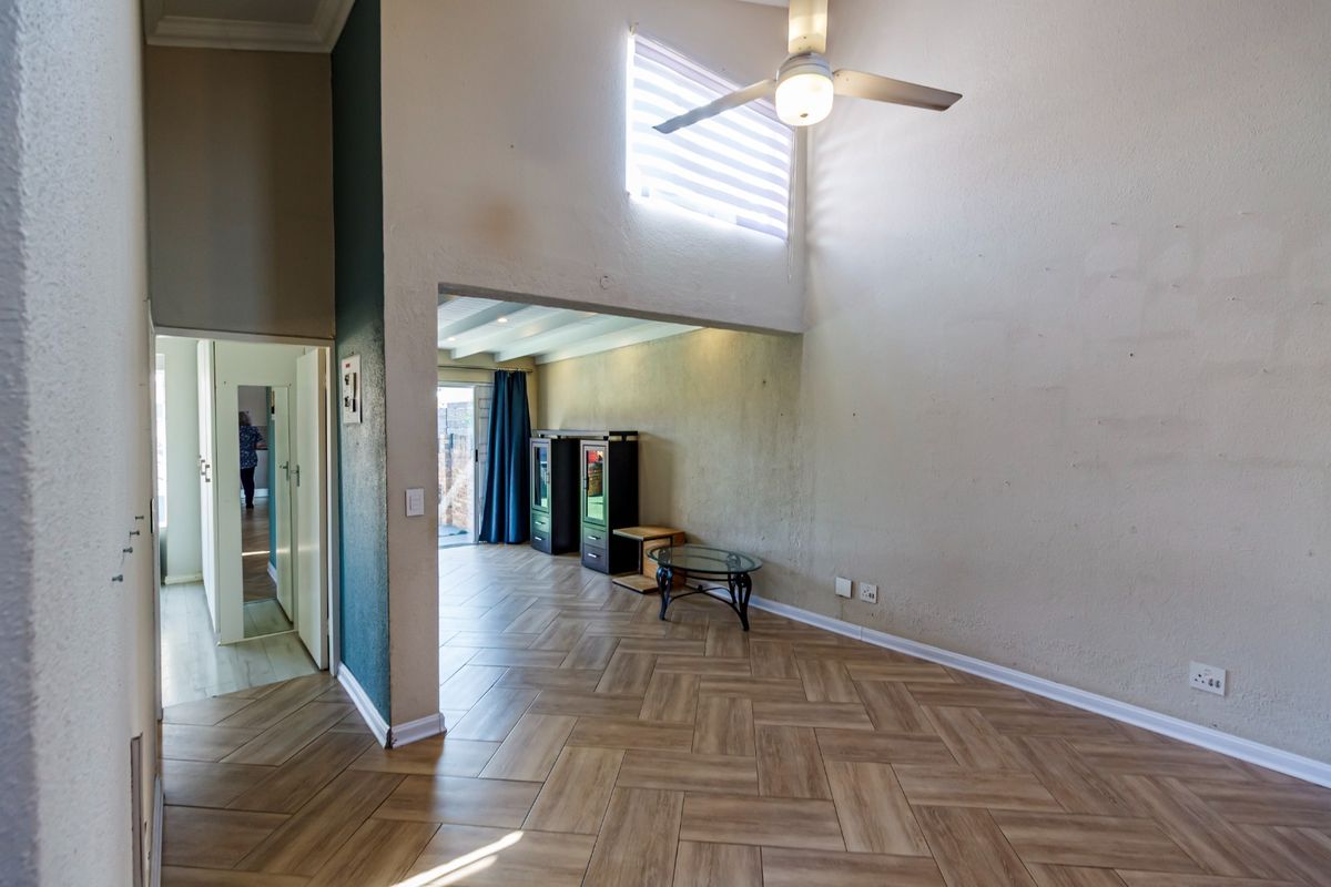 Spacious living area featuring double volume ceilings, a ceiling fan, and modern herringbone tile flooring with access to an adjoining room.