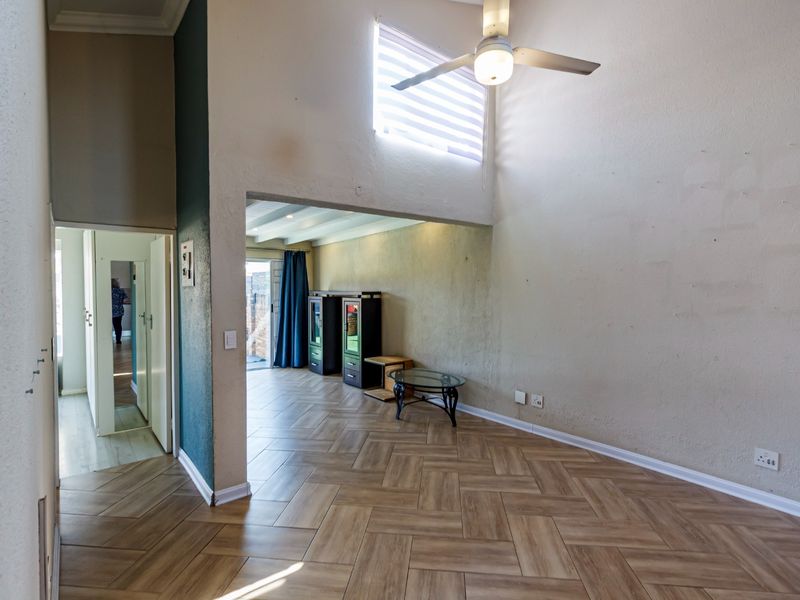 Spacious living area featuring double volume ceilings, a ceiling fan, and modern herringbone tile flooring with access to an adjoining room.