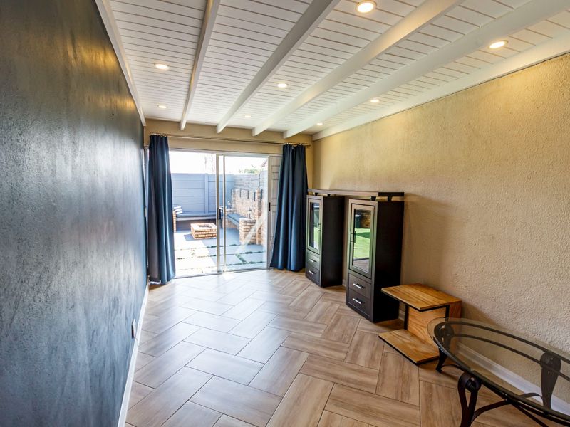 A bright living room featuring herringbone tile flooring, a textured accent wall, and a sliding glass door leading to an outdoor patio area.