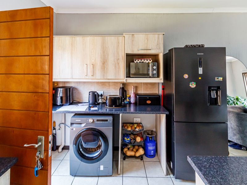 Compact kitchen area featuring laminate cabinetry, tiled backsplash, and dedicated space for laundry appliances and a refrigerator.
