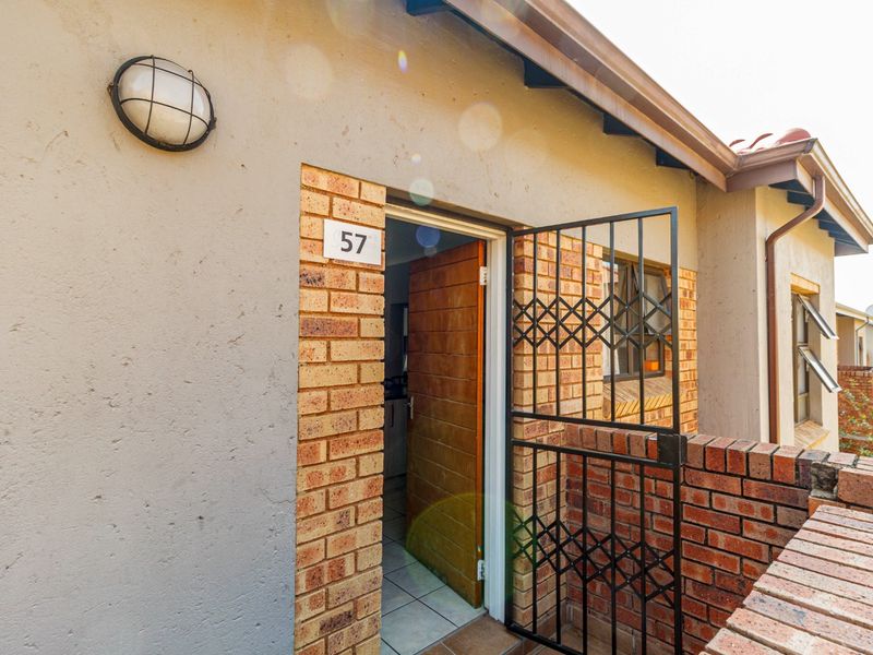 Entrance to apartment 57 featuring a brick facade, security gate, and exterior wall lighting.