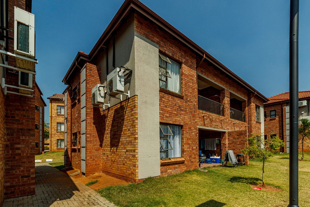 Exterior view of a multi-story face brick apartment building featuring concrete accents, external air conditioning units, and a paved walkway.