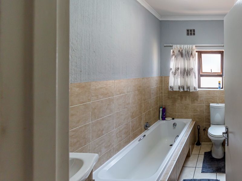 A functional bathroom featuring a built-in bathtub, toilet, and neutral wall and floor tiling, offering a clean and practical layout.