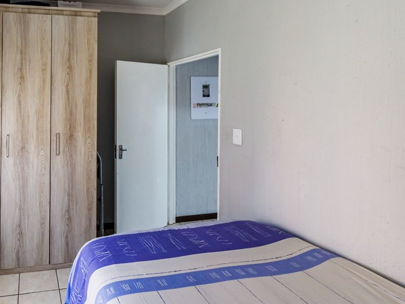 A bedroom featuring tiled flooring and a built-in wardrobe, with a view through the doorway into an adjacent space containing an electrical distribution board.