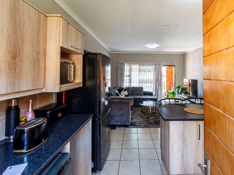 Open-plan kitchen and living area featuring light wood-look cabinetry, dark countertops, tiled floors, and access to a balcony through a sliding glass door.