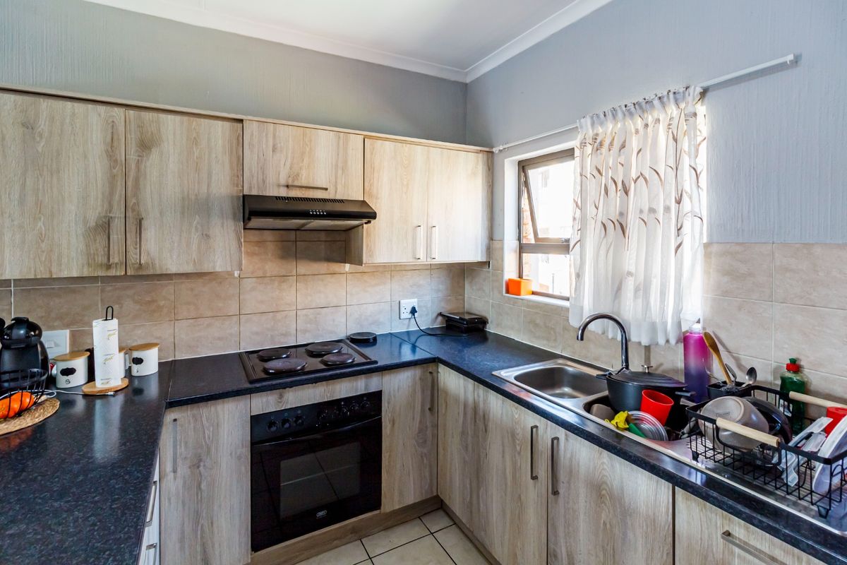 A functional kitchen featuring light wood-look cabinetry, dark countertops, a built-in oven with hob, and a tiled backsplash with a window for natural light.