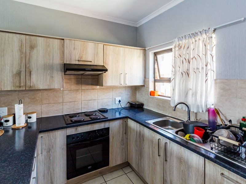 A functional kitchen featuring light wood-look cabinetry, dark countertops, a built-in oven with hob, and a tiled backsplash with a window for natural light.