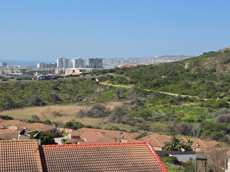 Elevated panoramic view overlooking the surrounding residential neighbourhood, natural landscape, and distant coastal city skyline.
