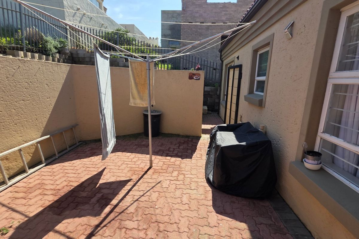 A paved rear courtyard area featuring a retaining wall and security-fitted windows, providing a functional outdoor utility space.