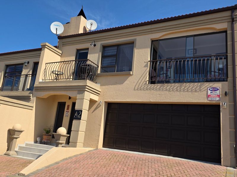 Front elevation of a multi-story residential property featuring a double garage, upper-level balconies with wrought iron railings, and a paved driveway.