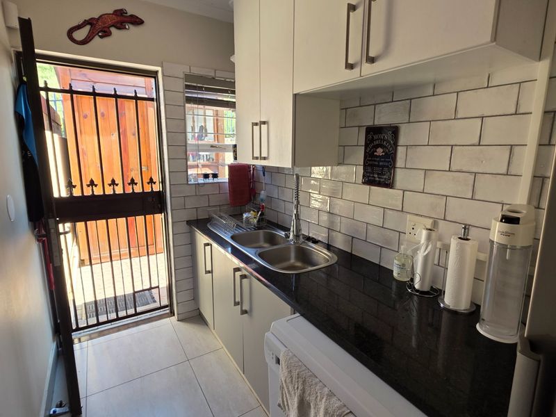 A functional scullery featuring granite countertops, a double bowl stainless steel sink, subway tile backsplash, and built-in cabinetry with direct exterior access.
