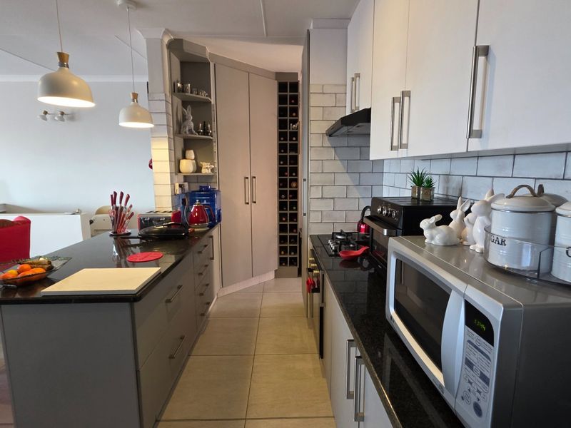 Modern kitchen featuring sleek grey and white cabinetry, granite countertops, subway tile backsplash, and a dedicated built-in wine rack.