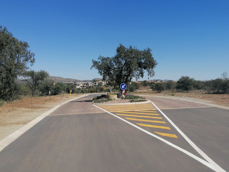 A view of a paved residential street featuring a traffic island with road markings and signage in a clear, sunny setting.