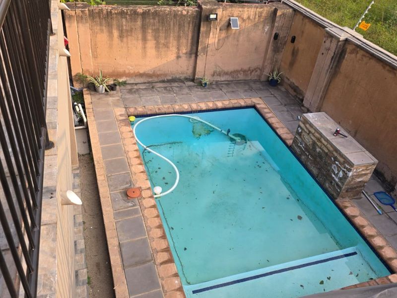 Outdoor pool area featuring a swimming pool, paved surround, built-in braai, and perimeter wall with electric fencing.