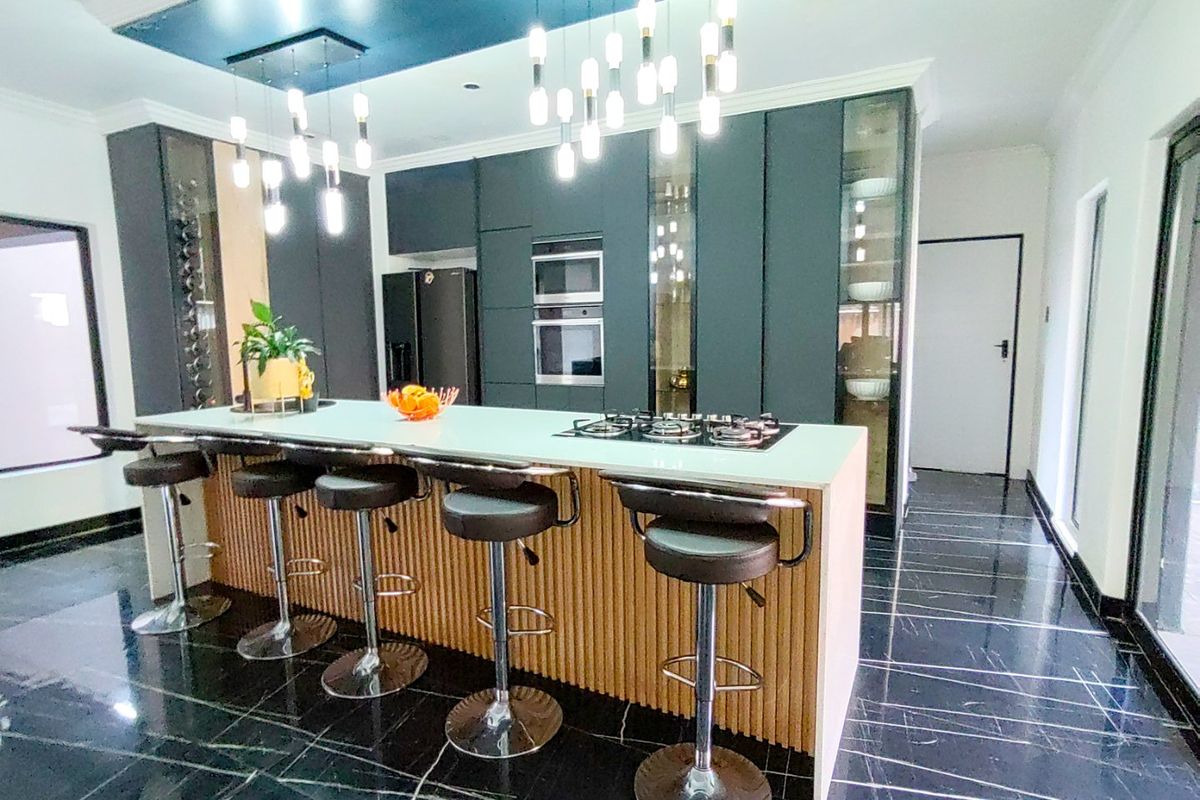 Modern kitchen featuring a large island with a gas hob, sleek dark cabinetry, built-in appliances, and elegant pendant lighting over a marble-look tiled floor.