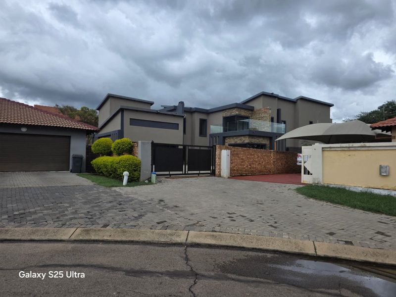 Front elevation of a modern multi-story house featuring stone cladding, a glass balcony, paved driveway, and secure gated entrance.