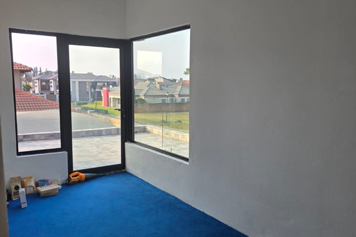 An empty, bright living area featuring large windows, a glass door leading to an outdoor space, and blue carpeting.