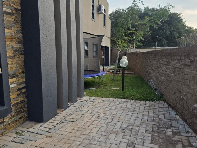 Rear exterior view featuring a paved patio area, stone-clad architectural pillars, and a garden space enclosed by a boundary wall.