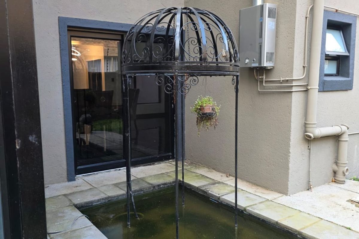 Rear exterior area featuring a small water feature, gas geyser installation, and paved flooring adjacent to a sliding door entrance.