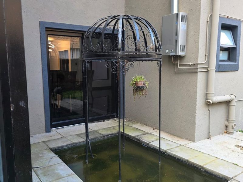 Rear exterior area featuring a small water feature, gas geyser installation, and paved flooring adjacent to a sliding door entrance.