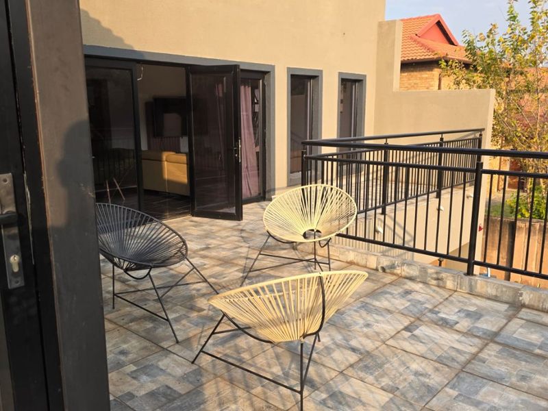 A spacious outdoor balcony featuring tiled flooring and a secure metal balustrade, accessible through double glass doors from the interior living space.