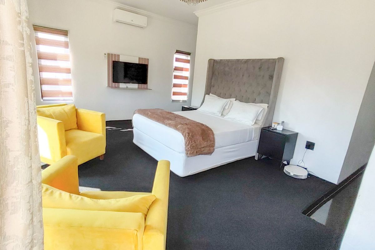 Spacious bedroom featuring a wall-mounted television, split-system air conditioning, modern zebra blinds, and a decorative chandelier.