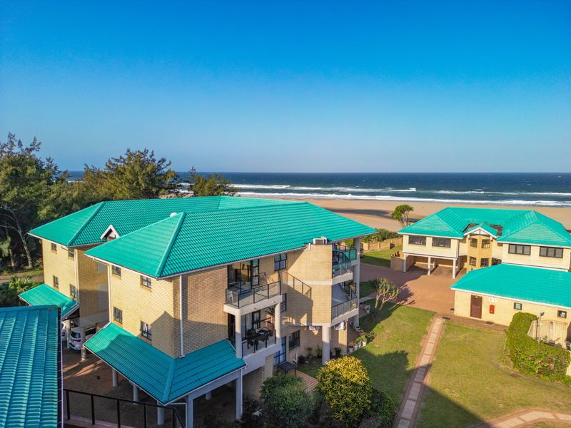 Aerial view of a coastal townhouse complex featuring green tiled roofs, brick facades, and direct proximity to the beach and ocean.