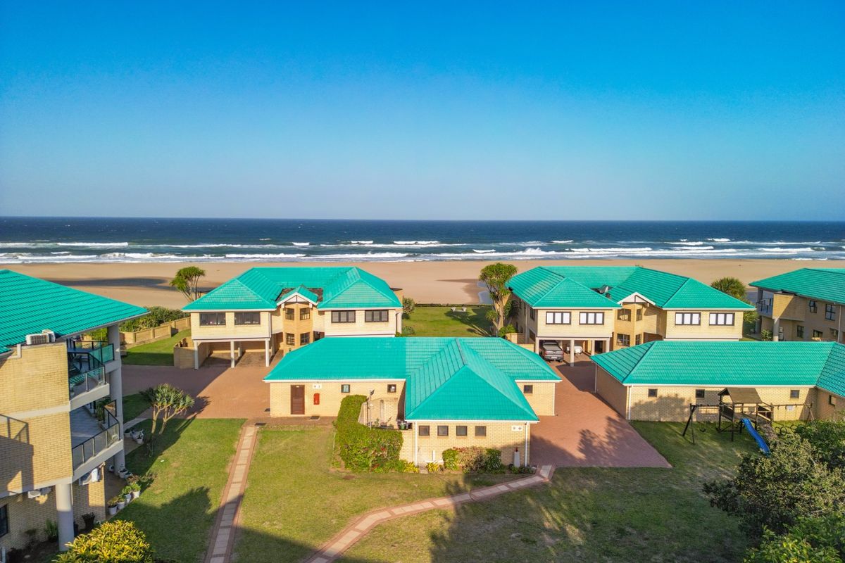 Aerial view of a beachfront townhouse complex featuring green tiled roofs, brick exteriors, paved driveways, and direct access to the beach.