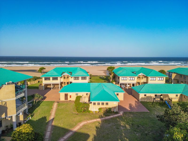 Aerial view of a beachfront townhouse complex featuring green tiled roofs, brick exteriors, paved driveways, and direct access to the beach.