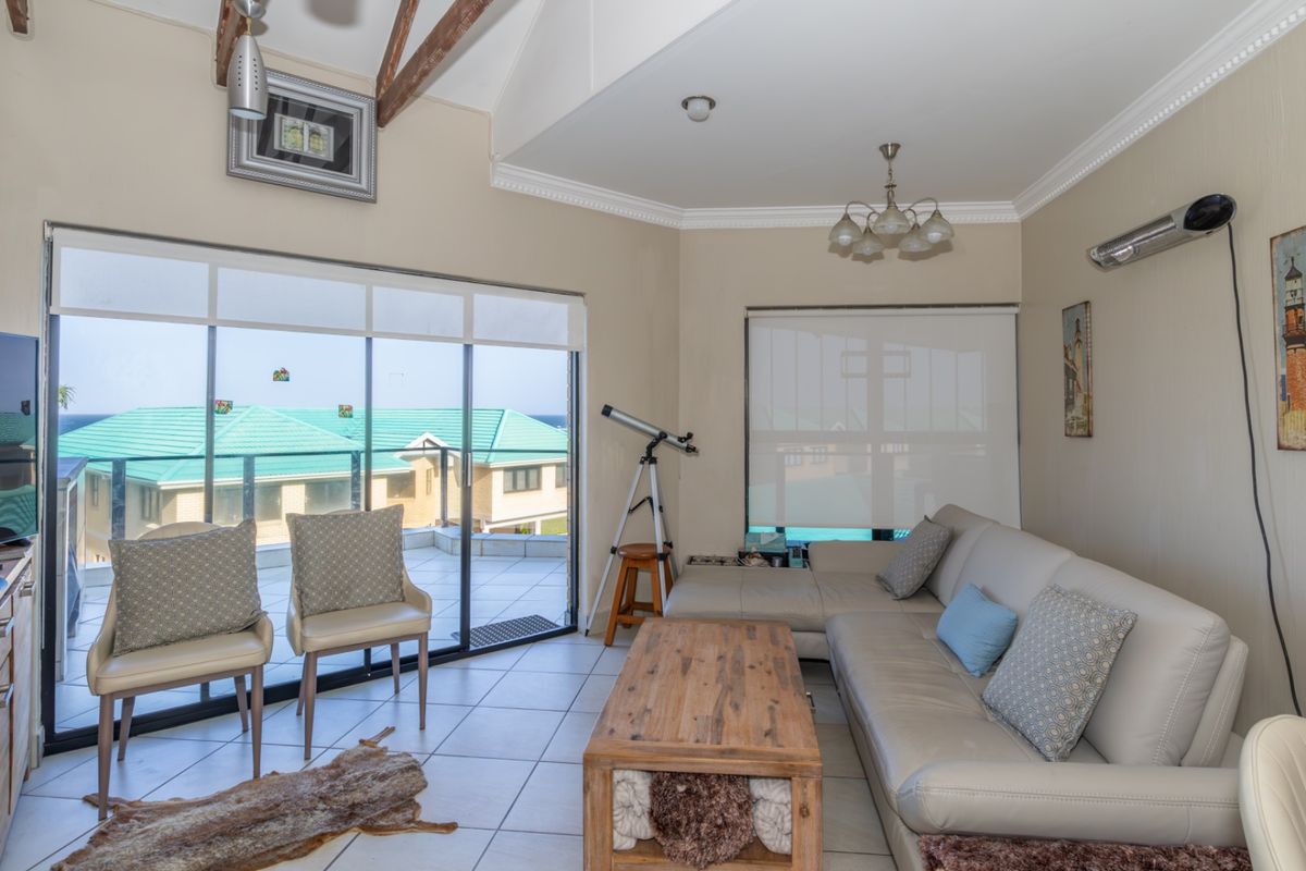 A bright living room featuring exposed timber ceiling beams, tiled flooring, and large sliding glass doors that open onto an outdoor balcony area.