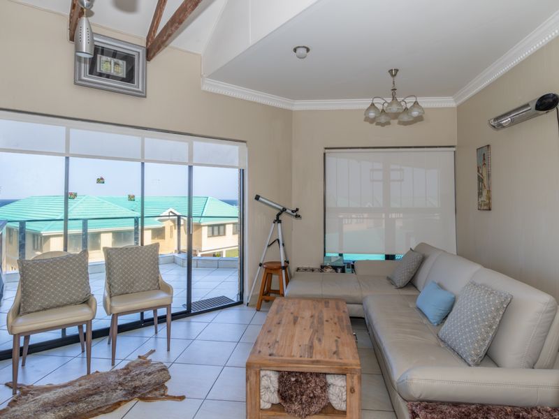 A bright living room featuring exposed timber ceiling beams, tiled flooring, and large sliding glass doors that open onto an outdoor balcony area.