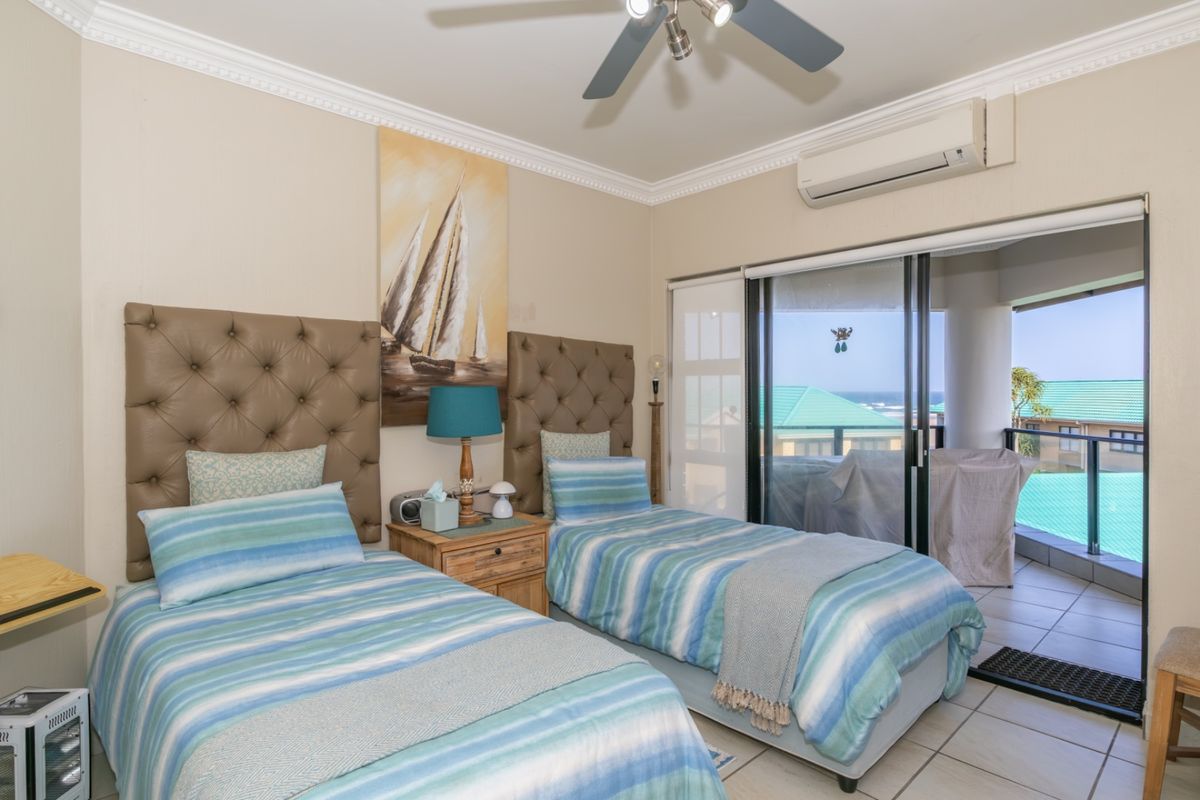 A well-maintained bedroom featuring tiled flooring, a ceiling fan, split-system air conditioning, and sliding glass doors leading to a private balcony with ocean views.