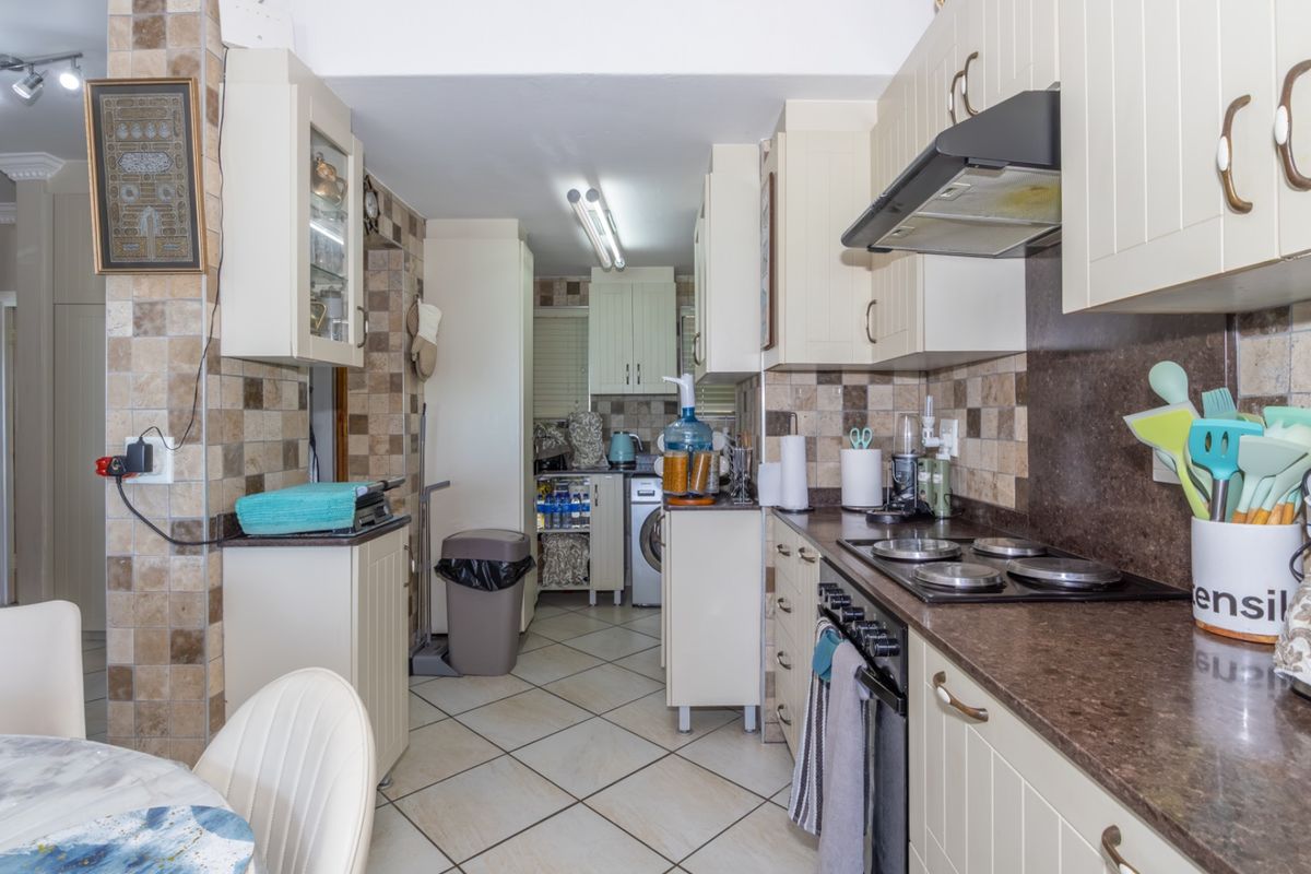A functional galley-style kitchen featuring cream cabinetry, dark laminate countertops, tiled backsplash, and integrated cooking appliances.