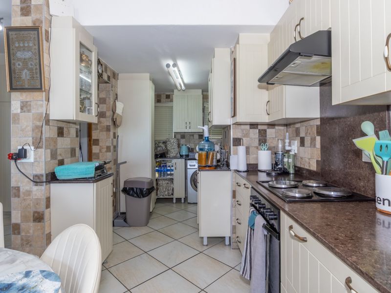 A functional galley-style kitchen featuring cream cabinetry, dark laminate countertops, tiled backsplash, and integrated cooking appliances.