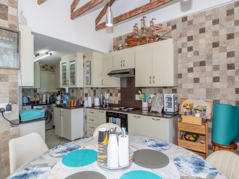 Open plan kitchen and dining area featuring exposed timber ceiling beams, tiled backsplash, and functional built-in cabinetry with integrated appliances.