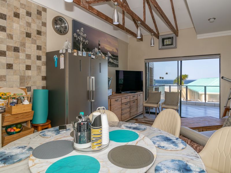 Open-plan living and dining area featuring exposed timber ceiling beams, a tiled feature wall, and sliding glass doors leading to a balcony with ocean views.