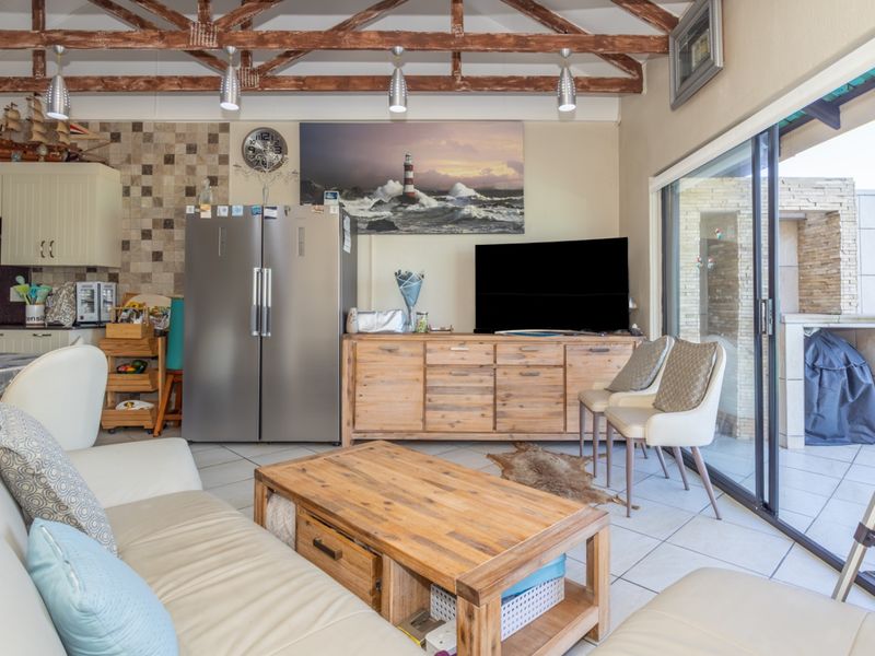 Open-plan living and kitchen area featuring exposed timber roof trusses, tiled flooring, and large sliding glass doors leading to an outdoor patio.
