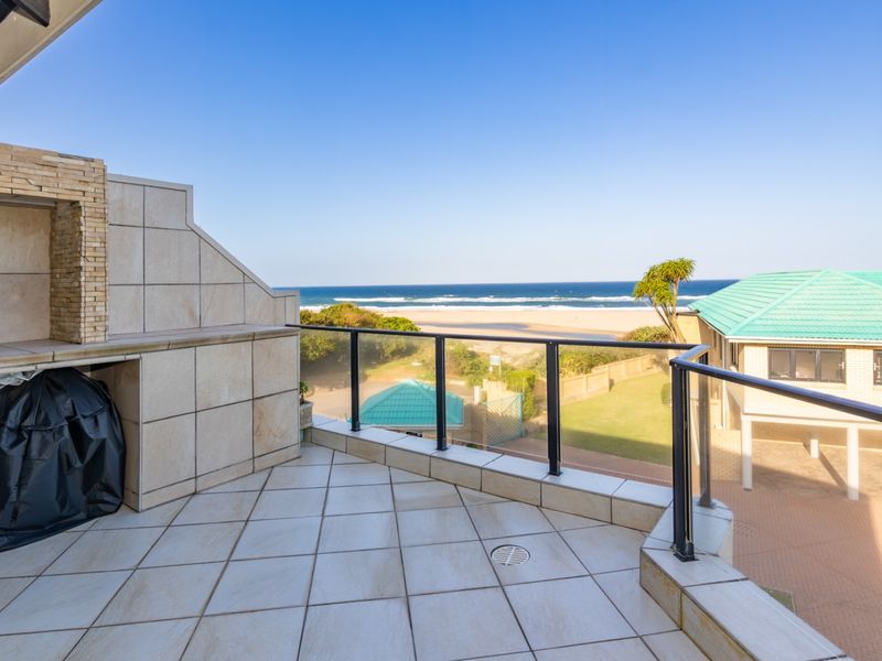 Spacious balcony featuring a built-in braai, tiled flooring, and a glass balustrade, offering expansive ocean and coastal views.