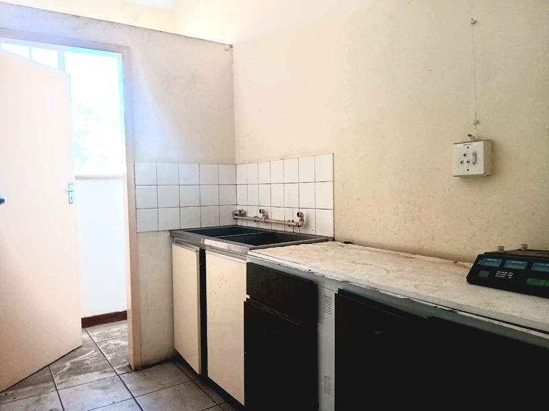 A basic, empty kitchen area featuring a stainless steel double sink, tiled splashback, and built-in cabinetry, requiring cosmetic updates and maintenance.