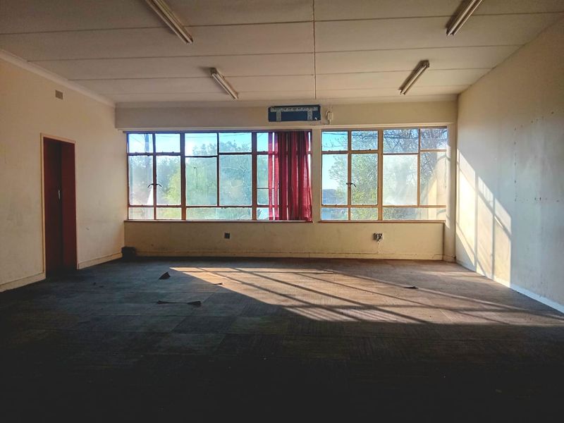 A vacant, open-plan office space featuring large windows, wall-mounted air conditioning, and fluorescent lighting, ready for refurbishment or custom fit-out.