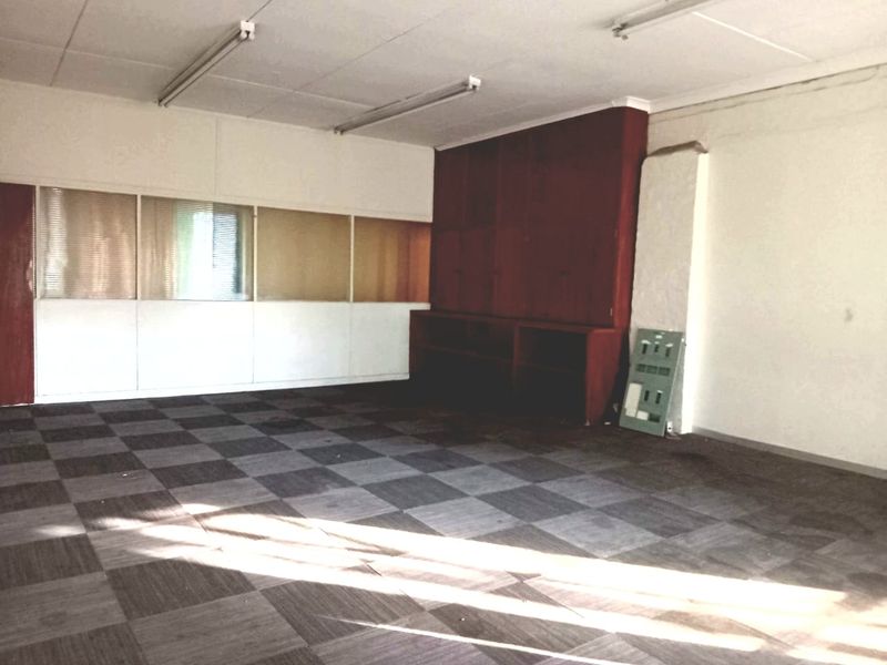 An empty commercial office space featuring built-in wooden cabinetry, fluorescent lighting, and modular carpet tiles, suitable for a professional workspace.