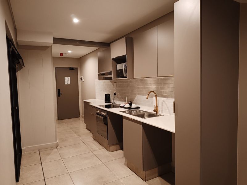 Modern kitchen featuring sleek cabinetry, stone countertops, integrated appliances, brass fixtures, and a tiled backsplash in a contemporary apartment setting.