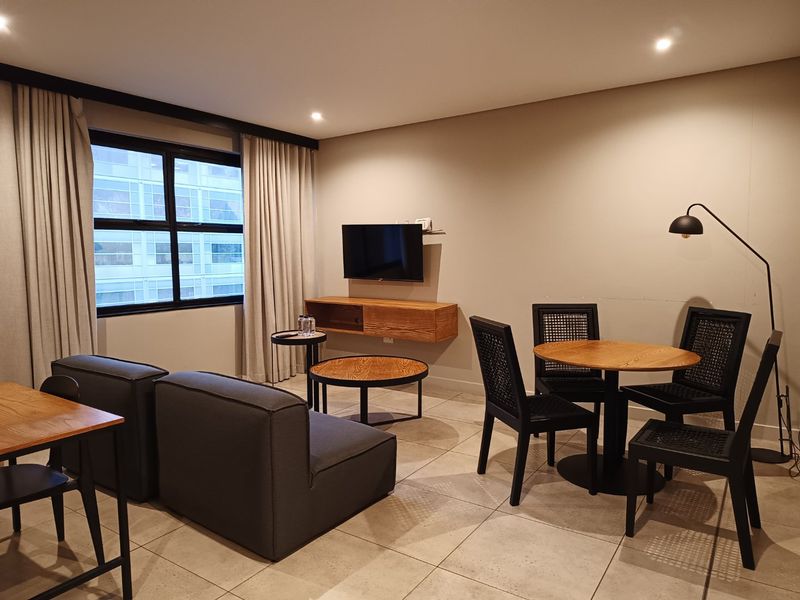 A well-maintained living area featuring tiled flooring, recessed lighting, and a wall-mounted media console, offering a clean and functional space.