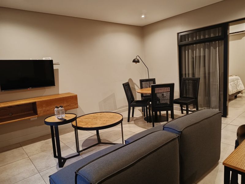A modern living room featuring tiled flooring, a wall-mounted media console, and a sliding glass door leading to an adjacent space.