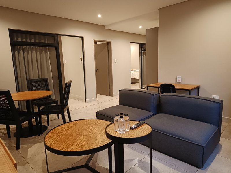 Open-plan living area featuring neutral wall tones, tiled flooring, and recessed lighting, providing a clean and functional space with access to adjacent rooms.